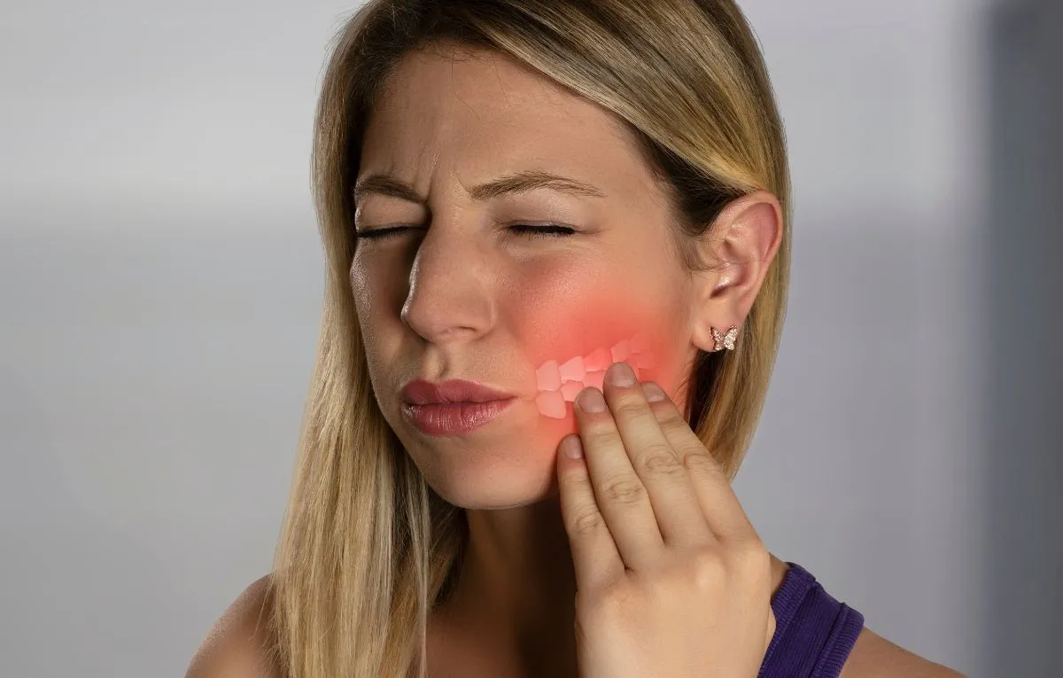 Mulher com a mão na bochecha sentindo dor de dente.